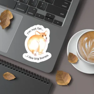 An image of a laptop with a sticker placed on the bottom right corner. The sticker is an illustration of an overweight corgi dog, with the text. 'I'm not fat - I like big bones.'